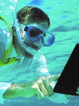 Homme sous l'eau avec masque et tuba consultant une tablette