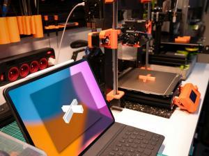 Ordinateur portable ouvert avec une croix modélisée en 3d. A droite, une imprimante 3d