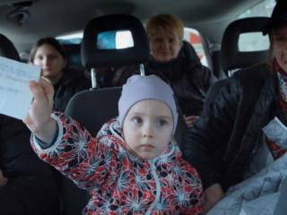 Une enfant est installée sur le siège arrière d'un van, entre deux adultes