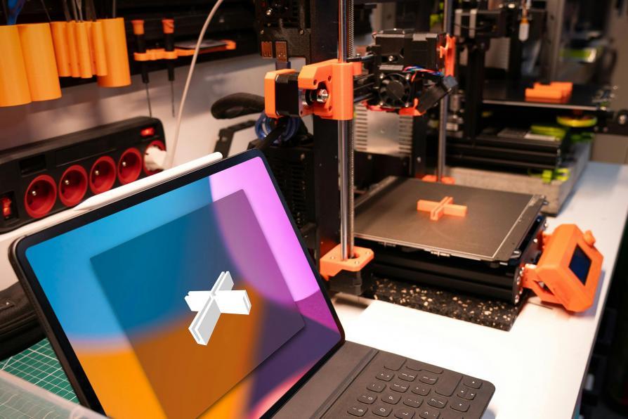 Ordinateur portable ouvert avec une croix modélisée en 3d. A droite, une imprimante 3d